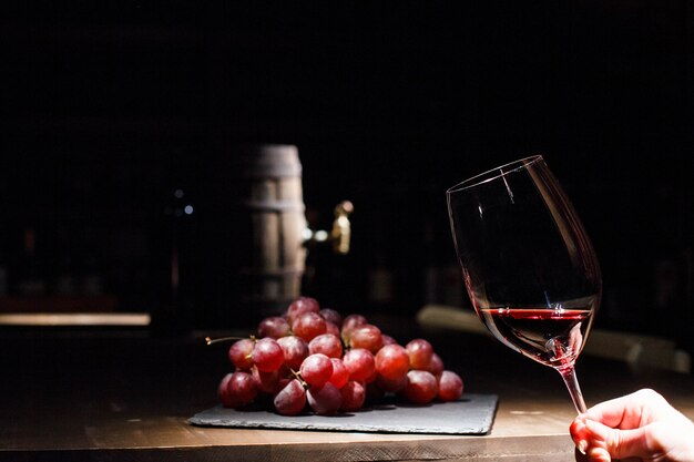 Frau hält Glas Wein vor Haufen Traube auf schwarzem Teller liegen