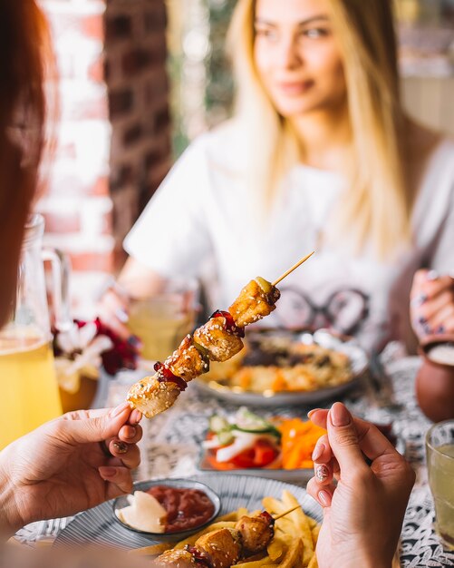 Frau hält Hühnerkebab auf Bambusspieß