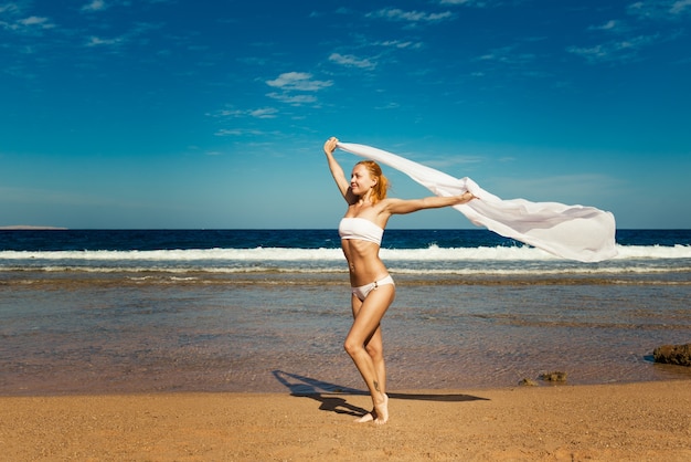 Frau hält weißen Schleier am Strand