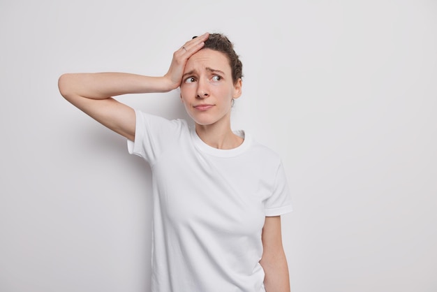 Kostenloses Foto frau hat kopfschmerzen wegen lebensproblemen sieht gestört aus hält hand auf kopf trägt lässige kleidung posiert auf weiß. oh nein wie kann das sein