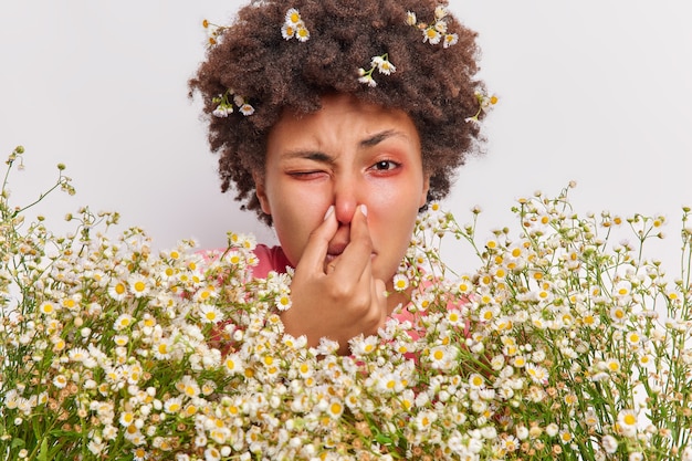 Frau hat Probleme mit der Atmung hält die Nase leidet an einer Kamille-Allergie hält großen Blumenstrauß hat rote juckende Augen