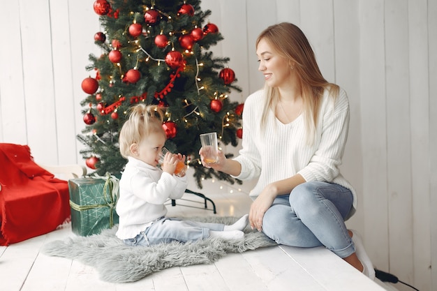 Frau hat Spaß, sich auf Weihnachten vorzubereiten. Mutter im weißen Pullover spielt mit Tochter. Die Familie ruht sich in einem festlichen Raum aus.