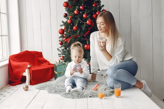 Frau hat Spaß, sich auf Weihnachten vorzubereiten. Mutter im weißen Pullover spielt mit Tochter. Die Familie ruht sich in einem festlichen Raum aus.