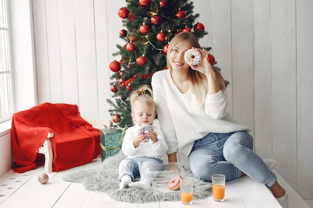 Frau hat Spaß, sich auf Weihnachten vorzubereiten. Mutter im weißen Pullover spielt mit Tochter. Die Familie ruht sich in einem festlichen Raum aus.