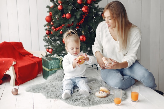 Frau hat Spaß, sich auf Weihnachten vorzubereiten. Mutter im weißen Pullover spielt mit Tochter. Die Familie ruht sich in einem festlichen Raum aus.