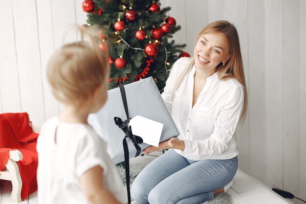 Frau hat Spaß, sich auf Weihnachten vorzubereiten. Mutter in einem weißen Hemd spielt mit ihrer Tochter. Die Familie ruht sich in einem festlichen Raum aus.