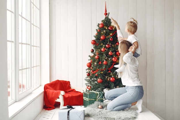 Frau hat Spaß, sich auf Weihnachten vorzubereiten. Mutter in einem weißen Hemd spielt mit ihrer Tochter. Die Familie ruht sich in einem festlichen Raum aus.