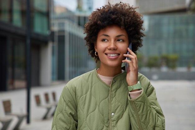 Frau hat Telefongespräch steht draußen im städtischen Umfeld zufrieden mit Tarifen im Roaming trägt Jacke