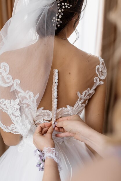 Frau hilft, Knöpfe am Hochzeitskleid der Braut zu befestigen