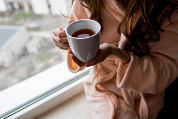 Frau im Bademantel, die Tasse heißen Tee hält. Herbststimmung.