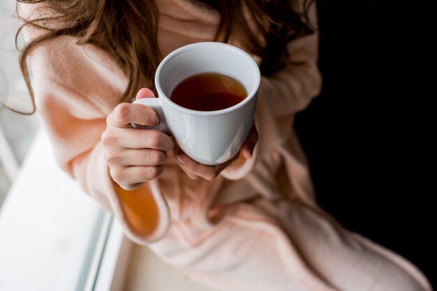 Frau im Bademantel, die Tasse heißen Tee hält. Herbststimmung.