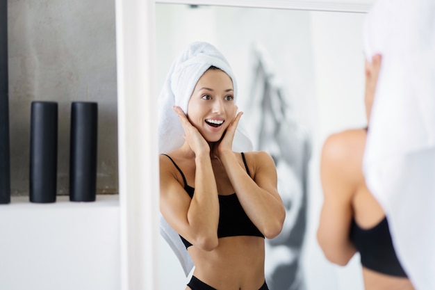 Frau im Badezimmer mit einem Handtuch auf dem Kopf vor einem Spiegel.
