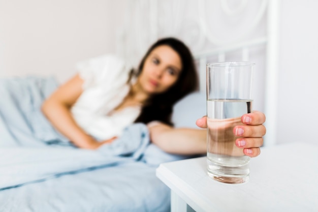 Frau im Bett, das Glas Wasser hält