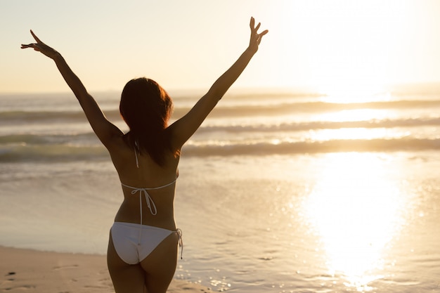 Kostenloses Foto frau im bikini, der mit den armen oben auf dem strand steht