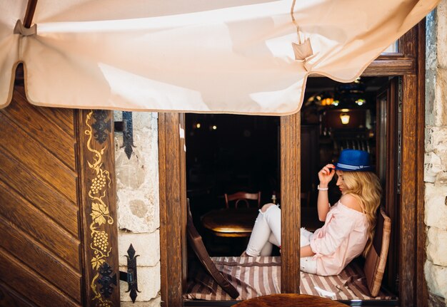 Frau im blauen Hut sitzt auf dem Fensterbrett im Café