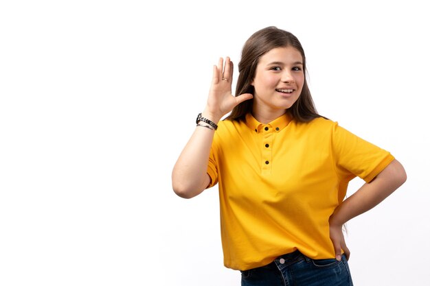 Frau im gelben Hemd und in den blauen Jeans, die mit glücklichem Ausdruck auf dem weißen Hintergrundfrauenmodellkleidung aufwerfen