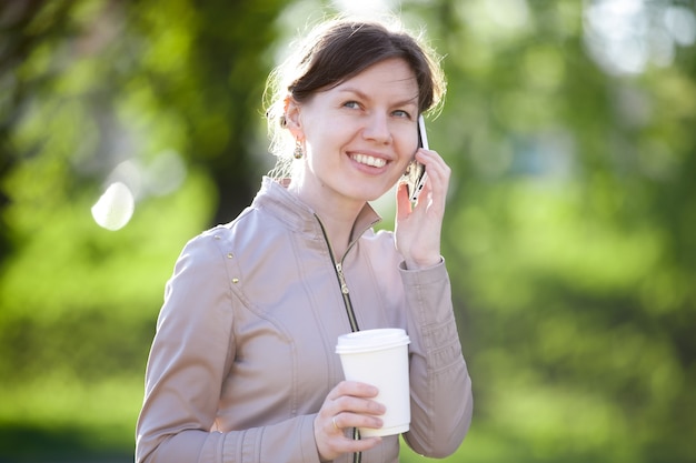 Frau im Gespräch über ihr Handy mit einem Kaffee