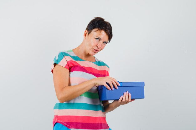 Frau im gestreiften T-Shirt, das versucht, Geschenkbox zu öffnen und neugierig schaut