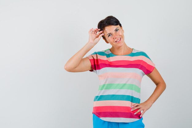 Frau im gestreiften T-Shirt, Hosen, die im Stehen aufwerfen und fröhlich schauen