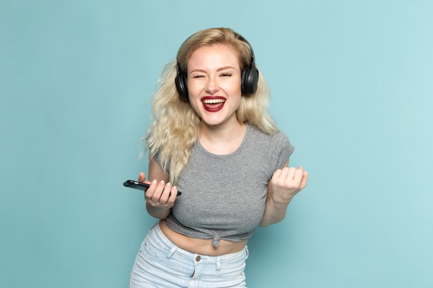 Frau im grauen Hemd und in den hellen blauen Jeans, die ein Telefon halten, das Musik hört