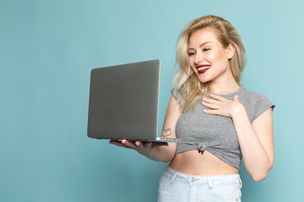 Frau im grauen Hemd und in den hellen blauen Jeans mit Laptop