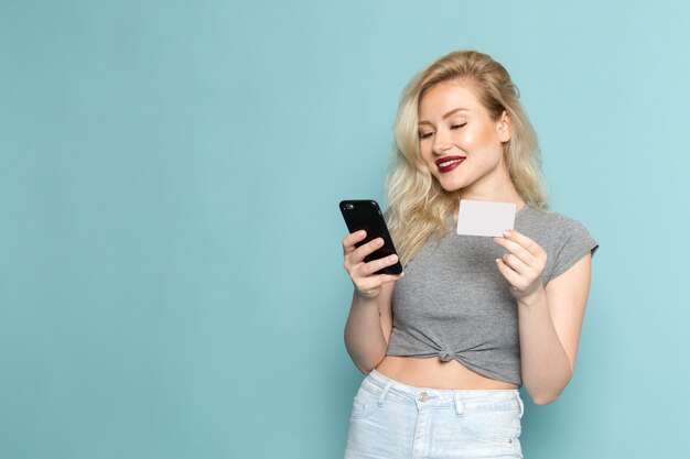 Frau im grauen Hemd und in den hellen blauen Jeans unter Verwendung eines Telefons