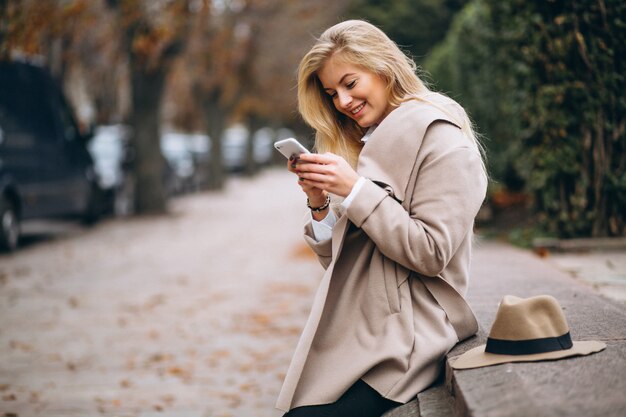 Frau im Hut und im Mantel im Park am Telefon sprechend