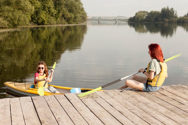 Frau im Kajak mit Freund, der Paddel auf Dock hält