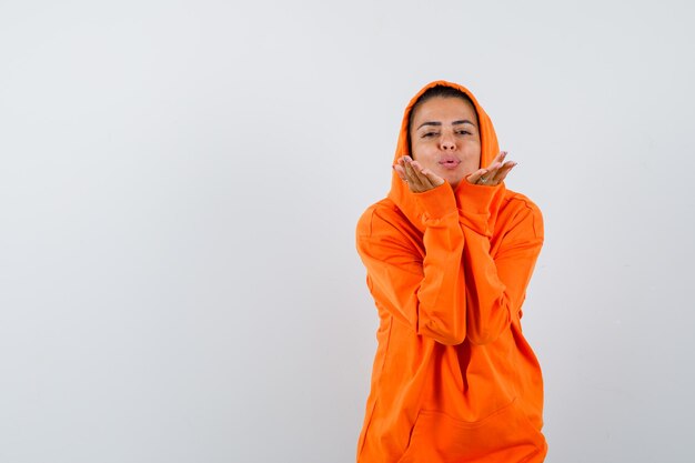 Frau im orangefarbenen Hoodie bläst Luftkuss mit schmollenden Lippen und sieht süß aus