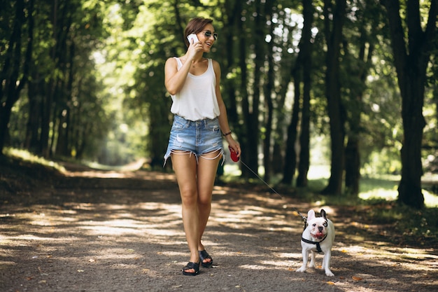 Frau im park mit der französischen bulldogge, die am telefon spricht