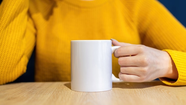 Frau im Pullover hält eine Tasse auf einem Holztisch