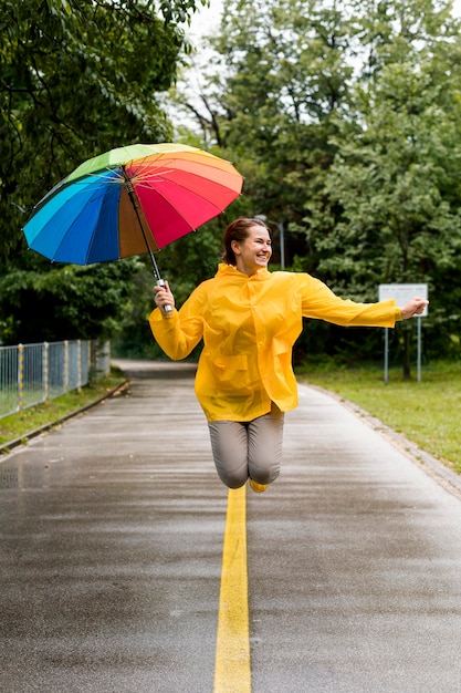 Frau im Regenmantel springend, während sie ihren Regenschirm hält