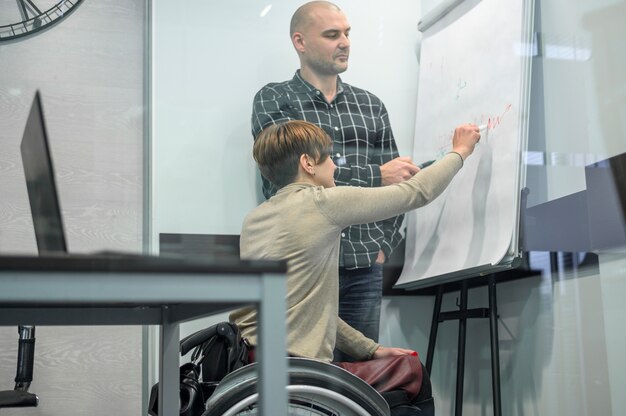 Frau im Rollstuhl, die auf einem Flipchart schreibt