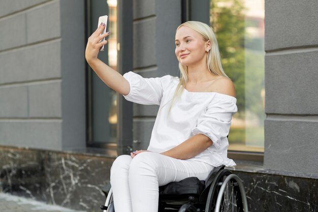 Frau im Rollstuhl, die selfie mit Smartphone nimmt