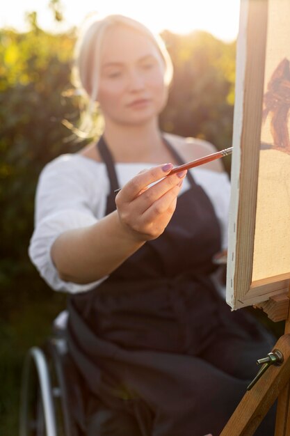 Frau im Rollstuhl mit Leinwand und Palette im Freien