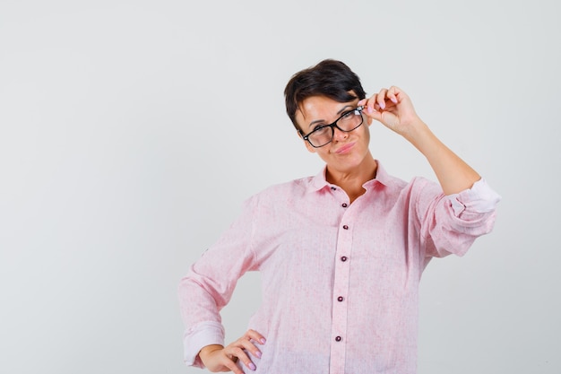 Frau im rosa Hemd, das beim Durchschauen der Brille aufwirft und nett, Vorderansicht schaut.