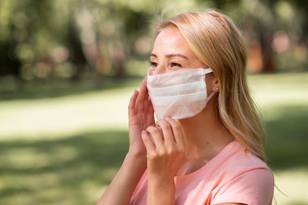 Frau im rosa T-Shirt, das medizinische Maske im Park trägt