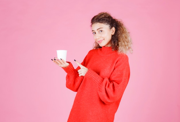 Frau im roten Hemd, das eine Wegwerfkaffeetasse hält.