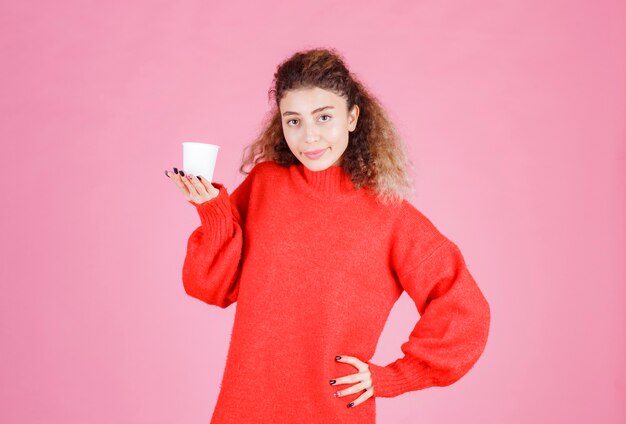 Frau im roten Hemd, das eine Wegwerfkaffeetasse hält.