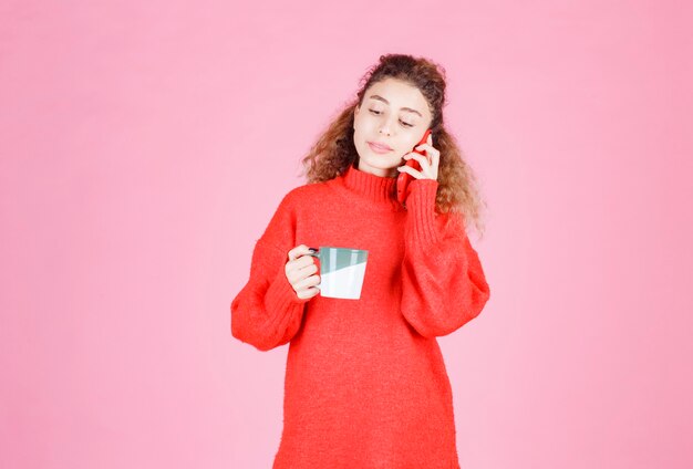 Frau im roten Hemd, die beim Kaffeetrinken mit dem Telefon spricht.