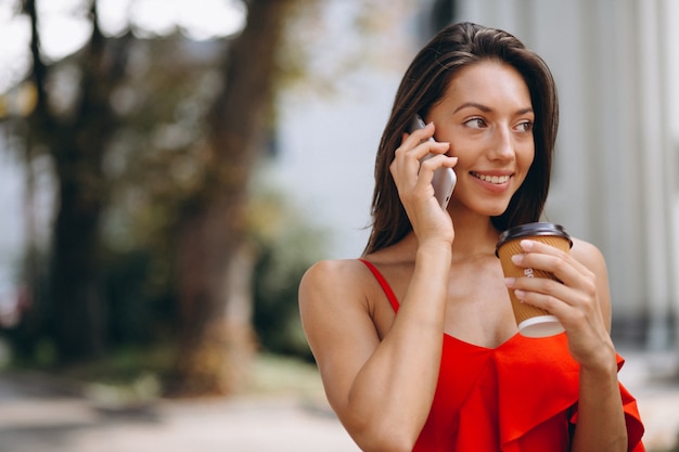 Frau im roten Kleid unter Verwendung des Telefons und des trinkenden Kaffees