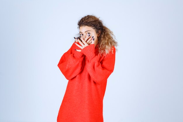 Frau im roten Sweatshirt, die über ihre Finger schaut.