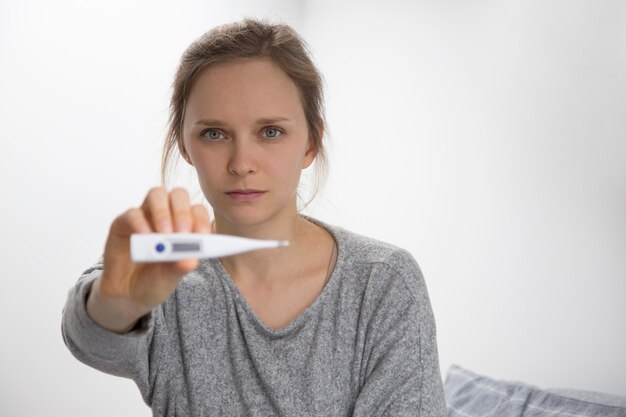 Frau im Schlafzimmer Thermometer demonstrierend, Kamera betrachtend