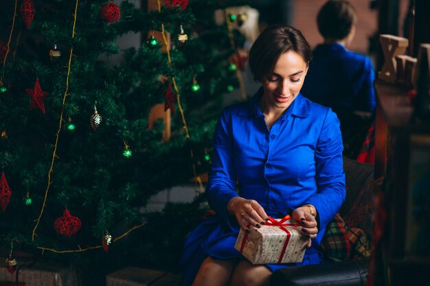 Frau im schönen Kleid, das durch Weihnachtsbaum sitzt