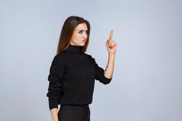 Frau im schwarzen Hemd, das mit dem Zeigefinger zeigt und jemanden schikaniert.