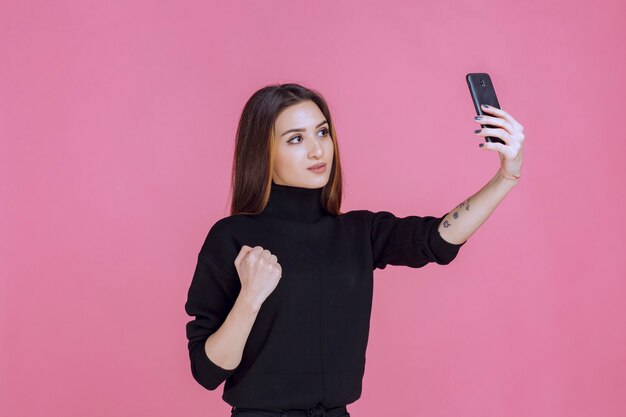 Frau im schwarzen Pullover, der ein Smartphone hält und ihr selfie nimmt.