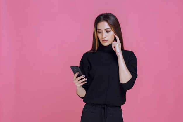 Frau im schwarzen Pullover hält ein Smartphone und SMS oder Überprüfung der sozialen Medien.
