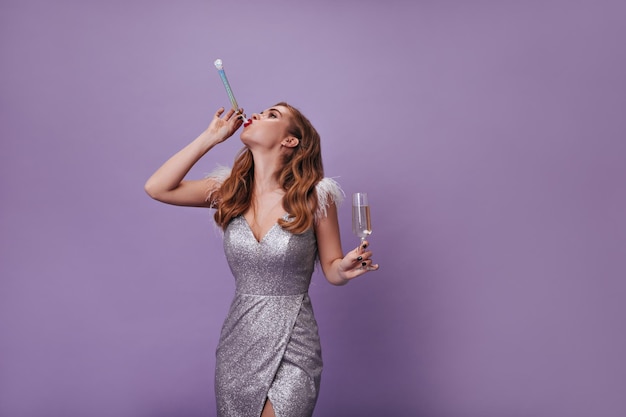 Frau im silbernen Kleid mit Partypfeife und Sektglas