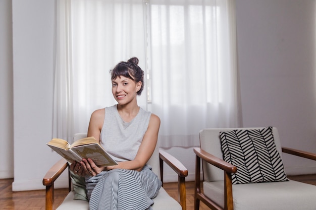 Frau im Stuhl ein Buch zu lesen und lächelnd