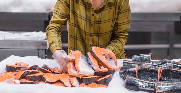 Kostenloses Foto frau im supermarkt. schöne junge frau, die einen lachsfisch in ihren händen hält.